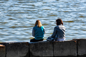Two teenage girls sit looking at sea in fall