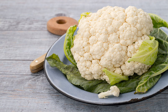 Fresh cauliflower on a round plate on an old wooden table. 