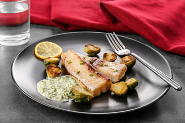 Plate with tasty fish and brussels sprouts on table
