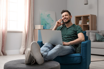 Young man working with laptop on armchair in home office