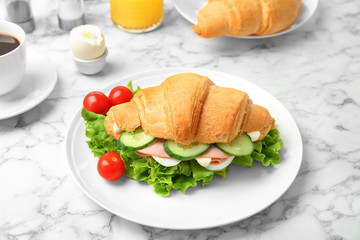 Tasty croissant sandwich with sausage on table
