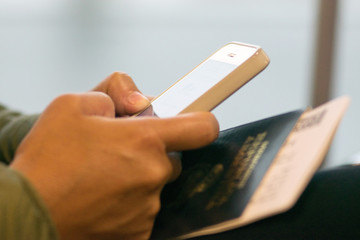Woman in waiting room of international airport, checking her phone with passport and phone