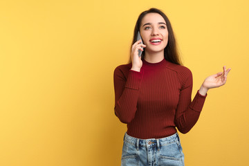 Young woman talking on phone against color background