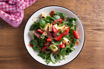 Strawberry, avocado, basil, mint, arugula salad with brie cheese and jamon or prosciutto. Healthy salad bowl. View from above, top studio shot
