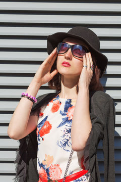 Closeup portrait of gorgeous young woman wearing hat and sunglasses, posing near the shutters in rays if sun