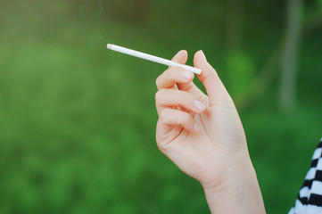 Cigarette in a female hand on a green background.