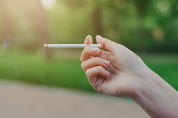 Cigarette in a female hand on a green background.