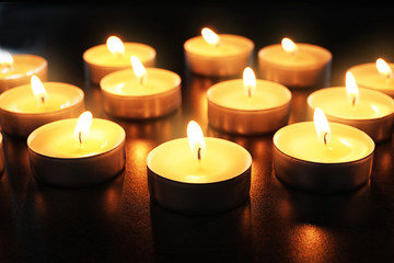 Fototapeta na wymiar Wax candles burning on table in darkness, closeup