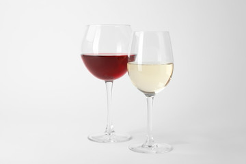 Glasses of expensive red and white wines on light background