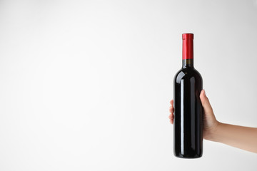 Woman holding bottle of expensive red wine on light background