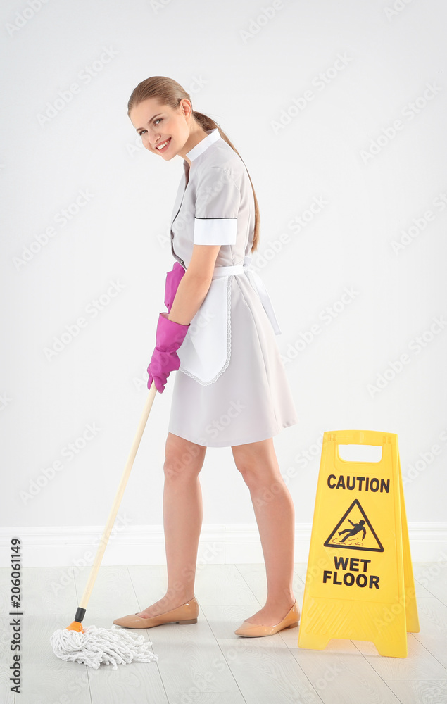 Poster Young chambermaid with mop near WET FLOOR sign indoors