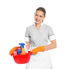 Young chambermaid holding basin with cleaning supplies on white background