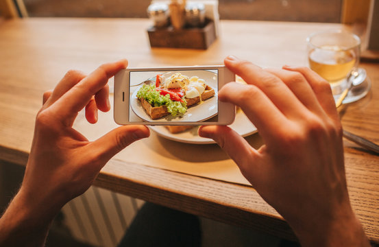 Man's hands is holding phone and taking picture of tasty meal on plate. It is colorful and delicious.