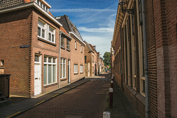 Working-class brick houses in a narrow empty street under sunny blue sky at Weesp. Quiet and pleasant village full of canals and green near Amsterdam. Northern Netherlands.