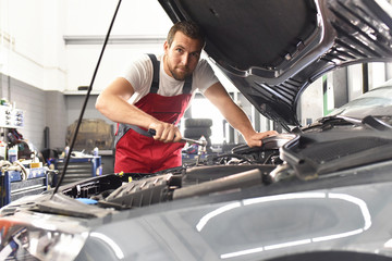 Portrait KFZ-Mechaniker repariert Auto in einer Werkstatt // Car mechanic repairs car in a workshop