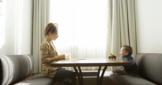 Young mother pretends to give son coffee in morning breakfast nook