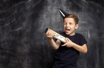 Little attractive boy with festive cap and flapper. Funny guy with slapstick in hands posing in...