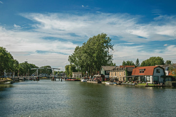 Fototapeta na wymiar Vecht River with bridge, boats on the banks and brick houses on a sunny day in Weesp. Quiet and pleasant village full of canals and green near Amsterdam. Northern Netherlands.
