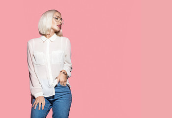 Blonde sexy woman in white shirt and jeans. Girl with glasses posing on a pink background. Studio...