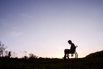 Obraz na płótnie Canvas A young man in wheelchair in nature in the evening.