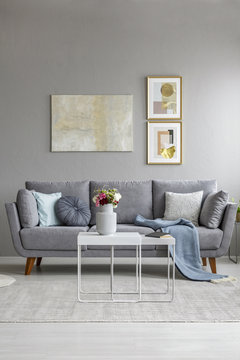 Flowers on table in front of grey couch in living room interior with poster on the wall. Real photo