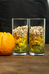 on a wooden table are two glasses with pieces of fruit. next door is a fresh orange. vertical photo.