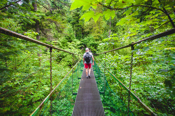The tourist is hiking through the suspension metal bridge with the chains. The canyon in the Tatras...