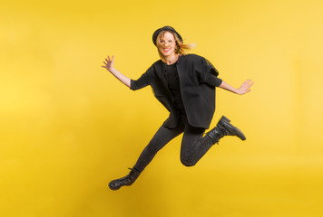 Fototapeta na wymiar Young beautiful woman with black hat in studio on a yellow background, jumping.