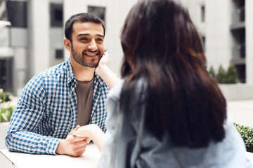 Happy couple touches their hands while sitting at table in cafe.