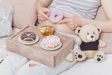 Pregnant woman with different colored donuts and a cup of tea