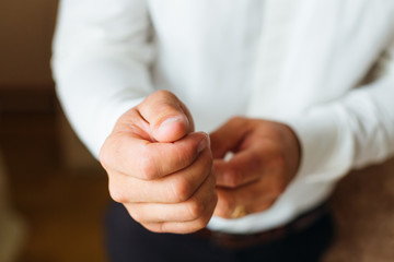 Close-up of the groom hands that holds the button on the cuffs of the white shirt