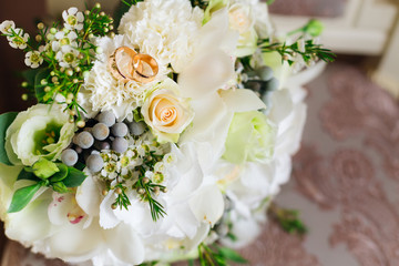 tender composition of white flowers and roses in a wedding bouquet and wedding rings on white petals