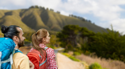 travel, tourism, hike and adventure concept - couple of travelers with backpacks over big sur hills of california background
