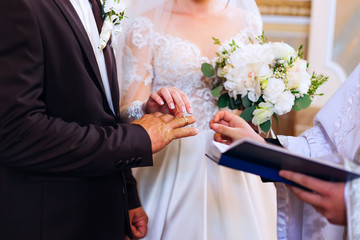 the bride and groom standing side by side in front of the priest and exchanging wedding rings