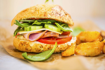 Ham burger or sandwich with ham slices,cheese, cucumbers, tomatoes and lettuce with wedges potatoes, rustic homemade sandwich