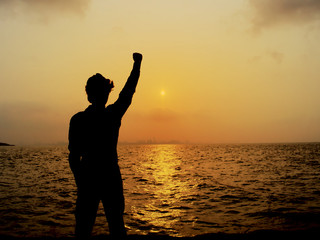 Fototapeta premium Silhouette of cheerful man raising hands during sunset over the sea. Successful concept.