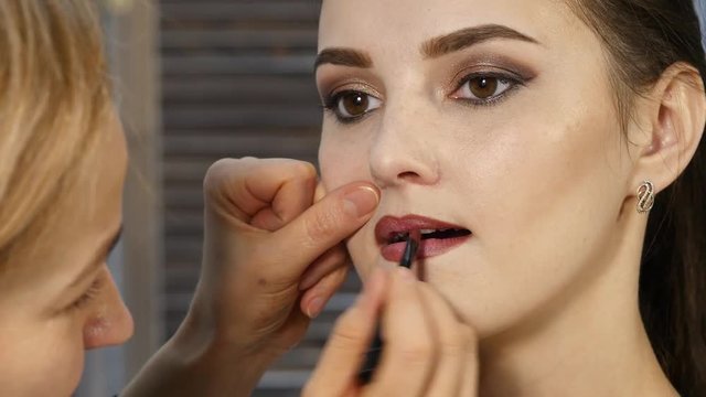 Female make-up artist apply pink lipstick with brush on a client lips