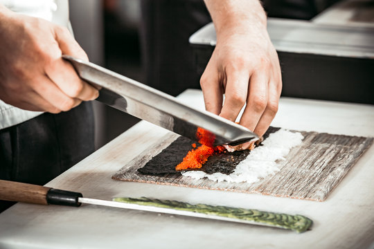 Close-up view of the man s hands cutting the caviar on the seaweed and rice layer. The professionals are making rolls for the tasty sushi in the modern restaurant.