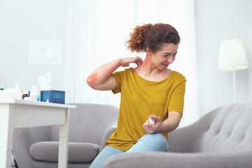 Sore neck. Young woman sitting on a grey couch suffering from a painful neck sprain giving her...