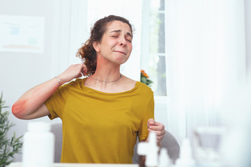 Neck rash. Young woman looking miserable and sore suffering from neck pain and allergic rash while trying to take off her necklace and apply some medication