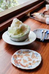 Japanses melon Kakigōri (shaved ice dessert) served in half of melon and sliced Pama Ham. With Dessert spoons in plate in background.