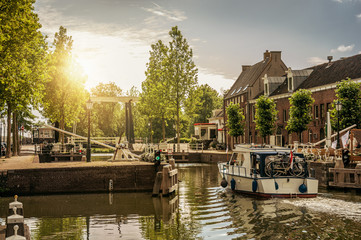 Boat passing by a tree-lined narrow canal in the sunrise at Weesp. Quiet and pleasant village full of canals and green near Amsterdam. Northern Netherlands. Retouched photo.