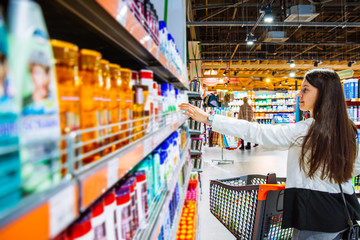 young woman in store with trolley. choose shampoo in supermarket. shopping concept. copy space