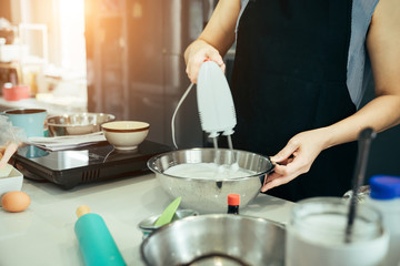 A woman using the mixture the cream for making the birthday cake for her family on weekend party.
