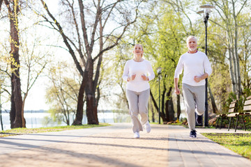 Active exercises. Positive senior couple jogging while being together in the morning