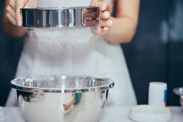 A woman sifting flour into a stainless bowl. Girl is sifting flour to making the bakery in her kitchen on weekend.