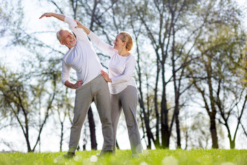 In shape. Positive active man doing an exercise while standing together with his trainer