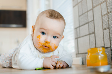 beautiful baby chest all dirty in fruit puree, pumpkin with spoon in hand next to a jar of food