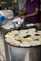 Crop shot of one kitchen helper frying some India flatbread, called Roti Prata, till they turned crispy and brown