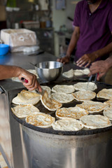 Crop shot of some kitchen helpers frying some India flatbread, called Roti Prata, till they turned crispy and brown
